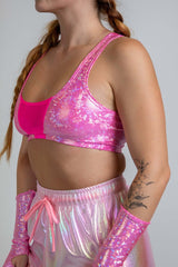 Model wearing a Bubble Gum Holo V Free Top, side view showcasing shiny pink holographic fabric with a strappy back, ideal for festivalss.