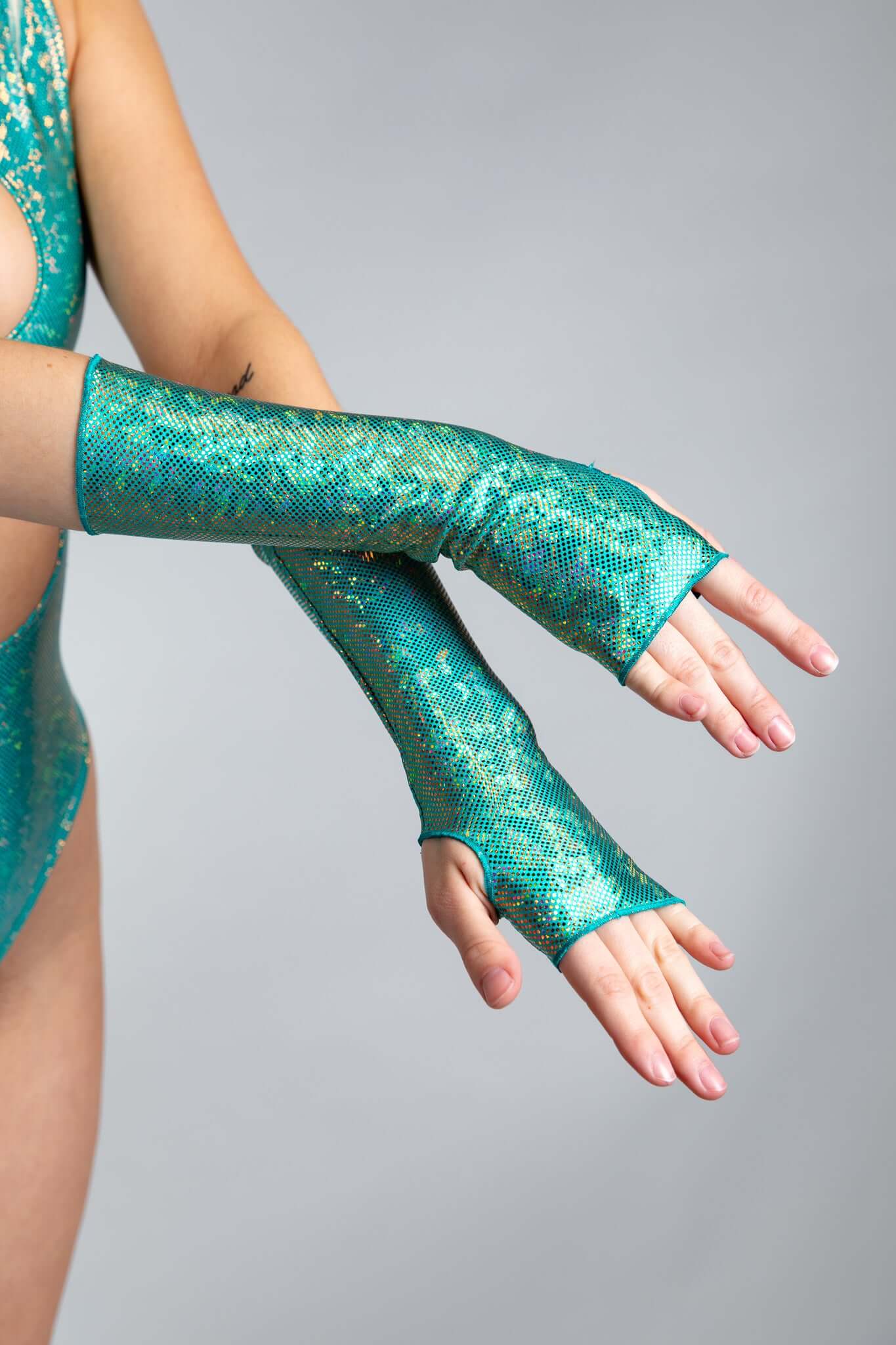 A woman's hands, crossed at the wrists, wearing holographic teal gloves.