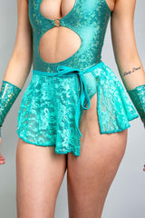 An up close photo of a woman wearing a teal, holographic bodysuit with two keyhole cutouts and a teal lace skirt that ties on the side.