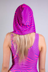 A woman with a hood and sleeveless bodysuit in pink and purple swirl patterns, featuring cut-out details. She is facing away from the camera.