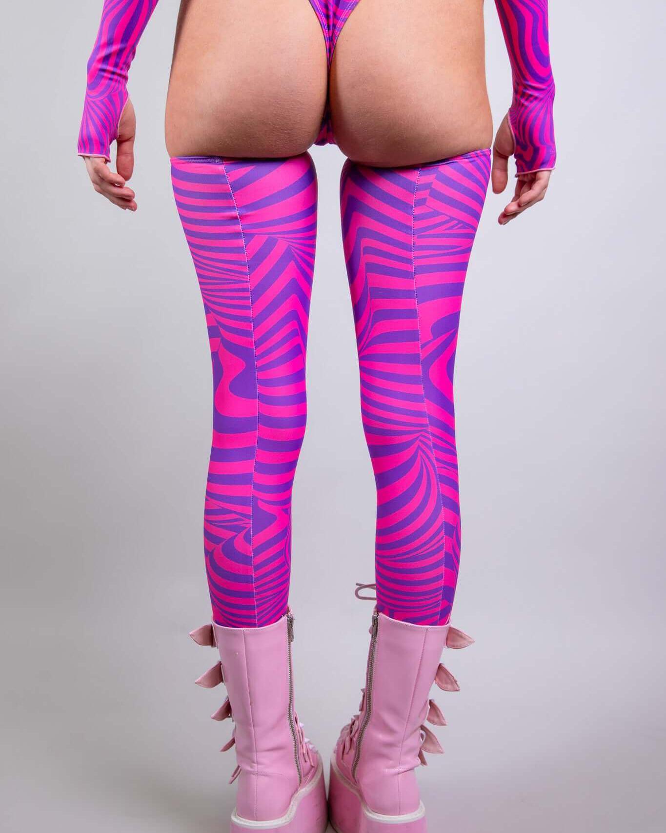 Model wearing vibrant pink Cheshire Leg Sleeves with a bold design, paired with chunky pink boots, perfect for rave outfits.