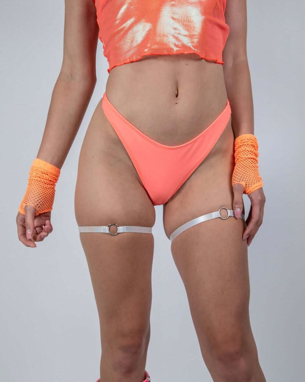 Woman wearing Valencia Risk Bikini Bottoms in neon coral, styled for rave outfits with accessories.