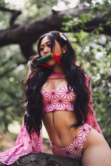Woman in a nature setting wearing a pink geometric rave top and sleeve, with playful hair clips and a mouth piece