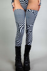 A woman's legs, wearing black boots and black and white geometric leg sleeves that go up to her upper thigh.