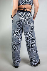 A person wearing wide legged pants with a black and white geometric pattern.  They are facing away from the camera.