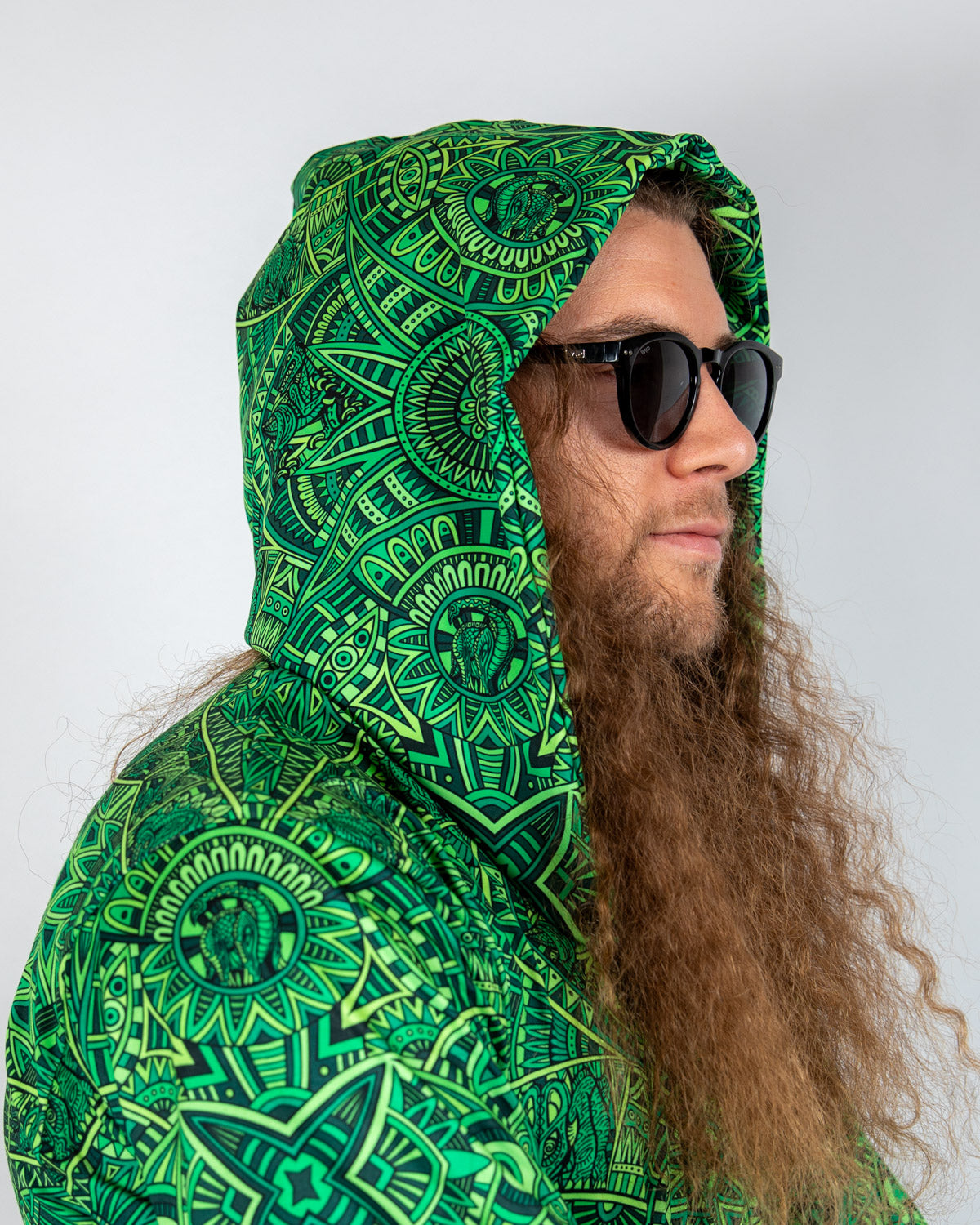 Model wearing green patterned Dominion Assassin Hood with oversized design and sunglasses, perfect for rave fashion.
