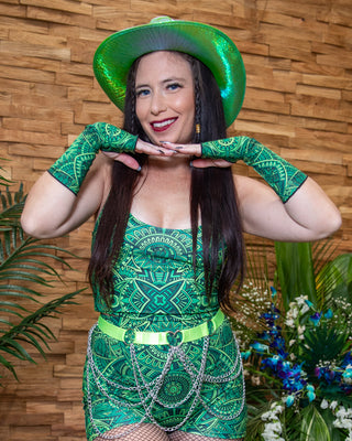 Young woman in green rave outfit and Dominion Gloves, posing with a vibrant hat and playful energy.