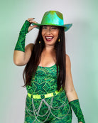 Woman wearing a green geometric outfit and rave gloves, smiling and sporting a shiny hat, perfect for festivals.