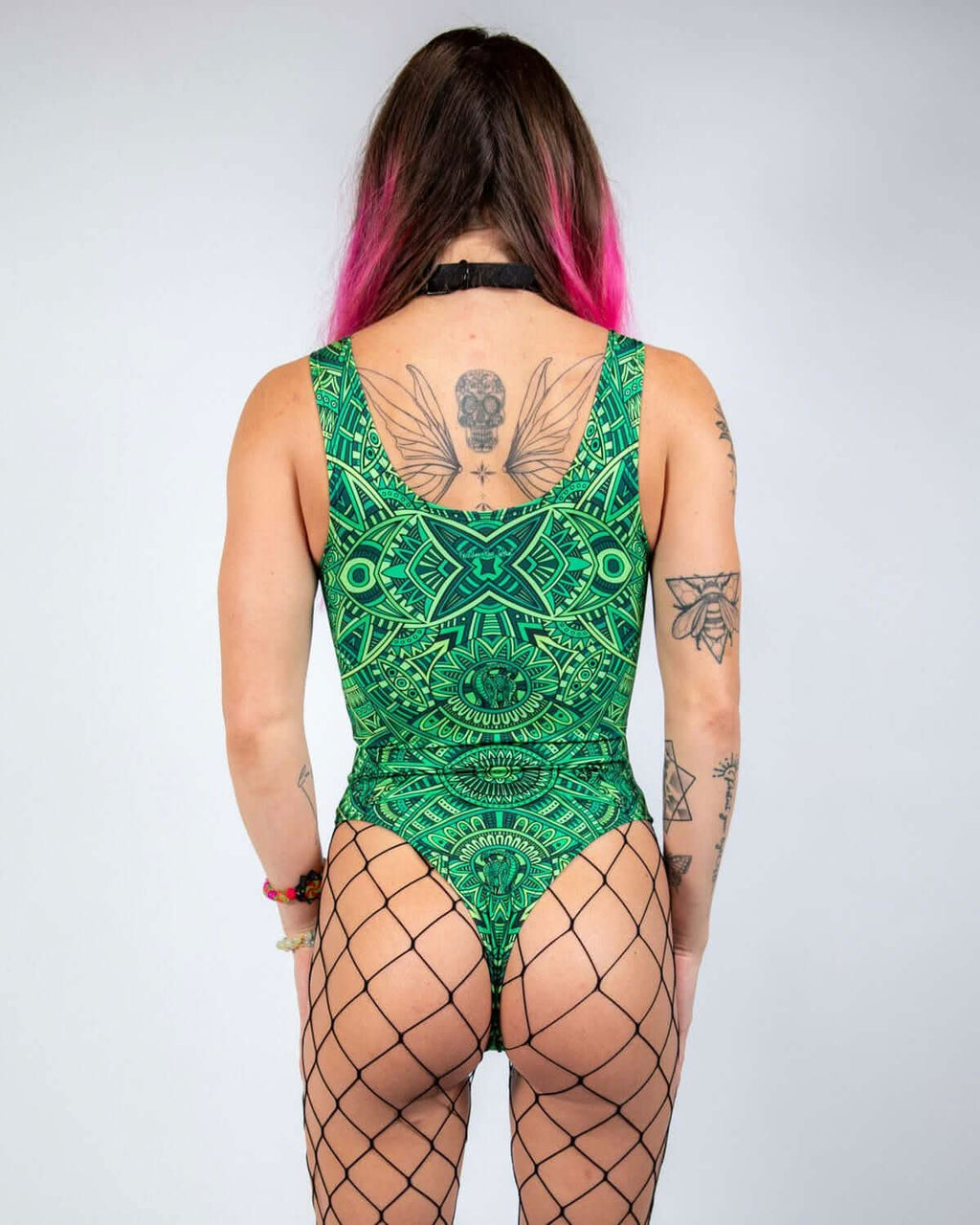 Model wearing a green Dominion Keyhole Bodysuit with intricate patterns, highlighted by fishnet stockings and vibrant hair.
