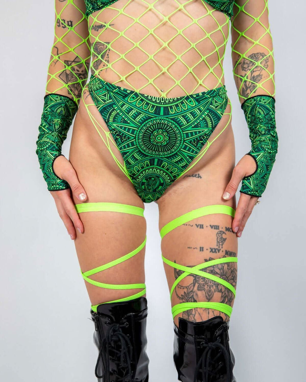 Dominion Retro Thong Bottoms featuring a green tribal design, high-cut leg, and paired with neon accessories for rave looks.