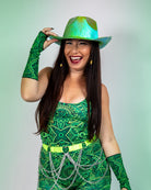 Woman in vibrant green rave outfit with a shiny hat, smiling energetically at the camera.
