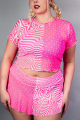 A woman wearing a mesh cropped pink and white t shirt and matching skirt.