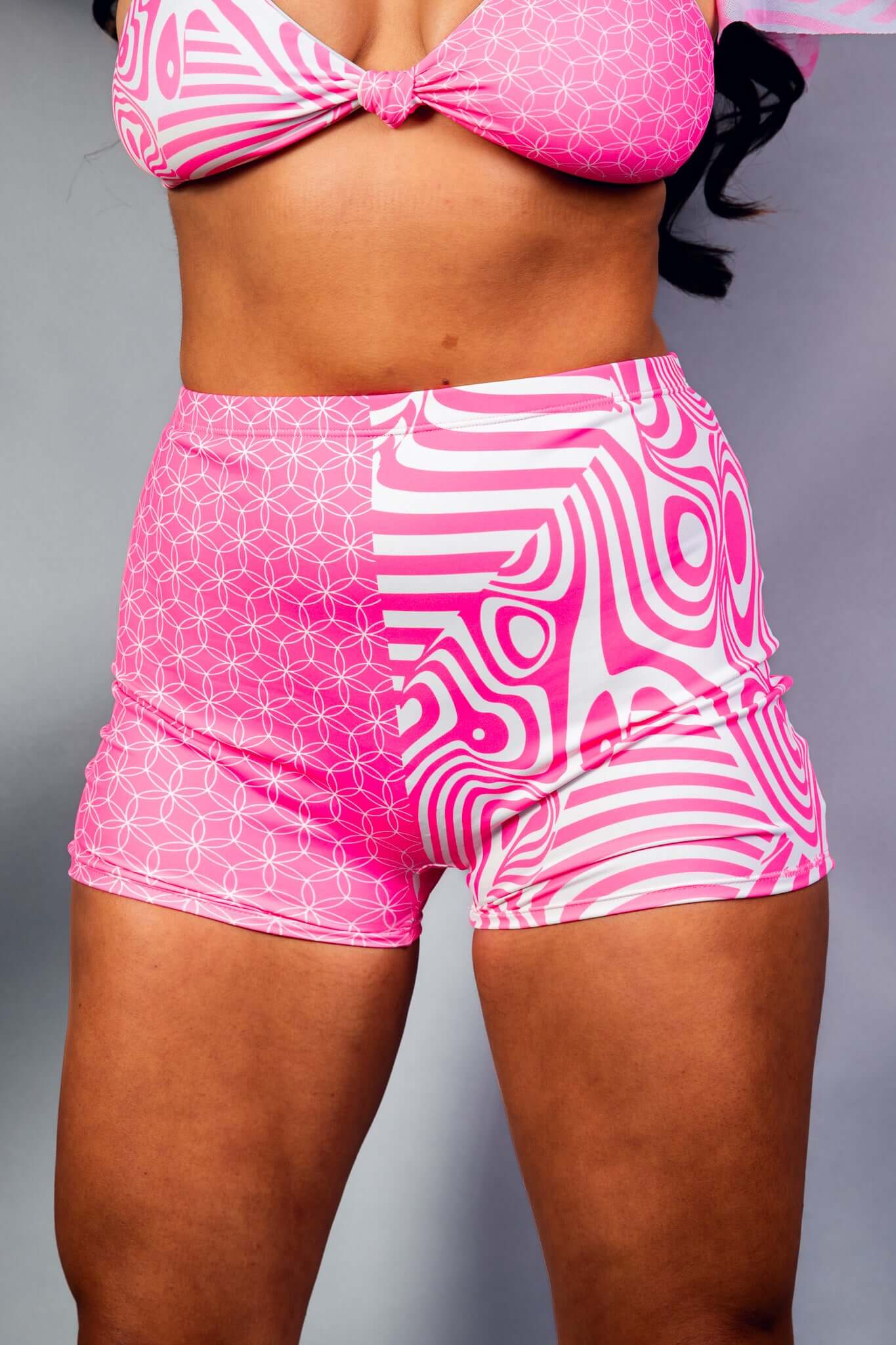 An up close photo of a woman wearing pink and white shorts with a matching crop top.