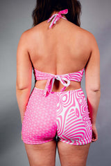 A woman wearing a pink and white halter top romper with a back tie. She is facing away from the camera.