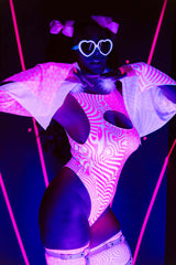 A woman wearing a pink and white bodysuit with matching sleeves that glow under the black light.