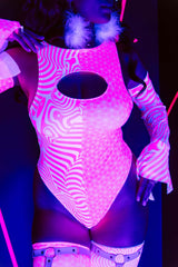 A woman standing under blacklight, wearing a pink and white bodysuit with a keyhole cutout, that glows under the light.