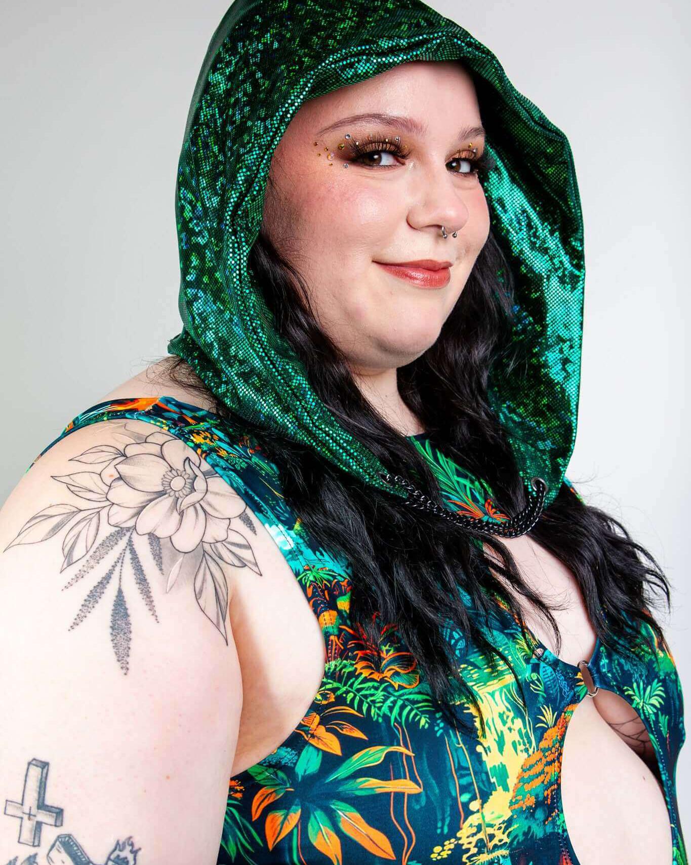 Model wearing an emerald holo assassin hood with chain, featuring a vibrant floral outfit, perfect for rave outfits.