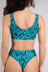 An up close photo of a woman wearing a blue and black swirl printed top with matching bikini bottoms. She is facing away from the camera.