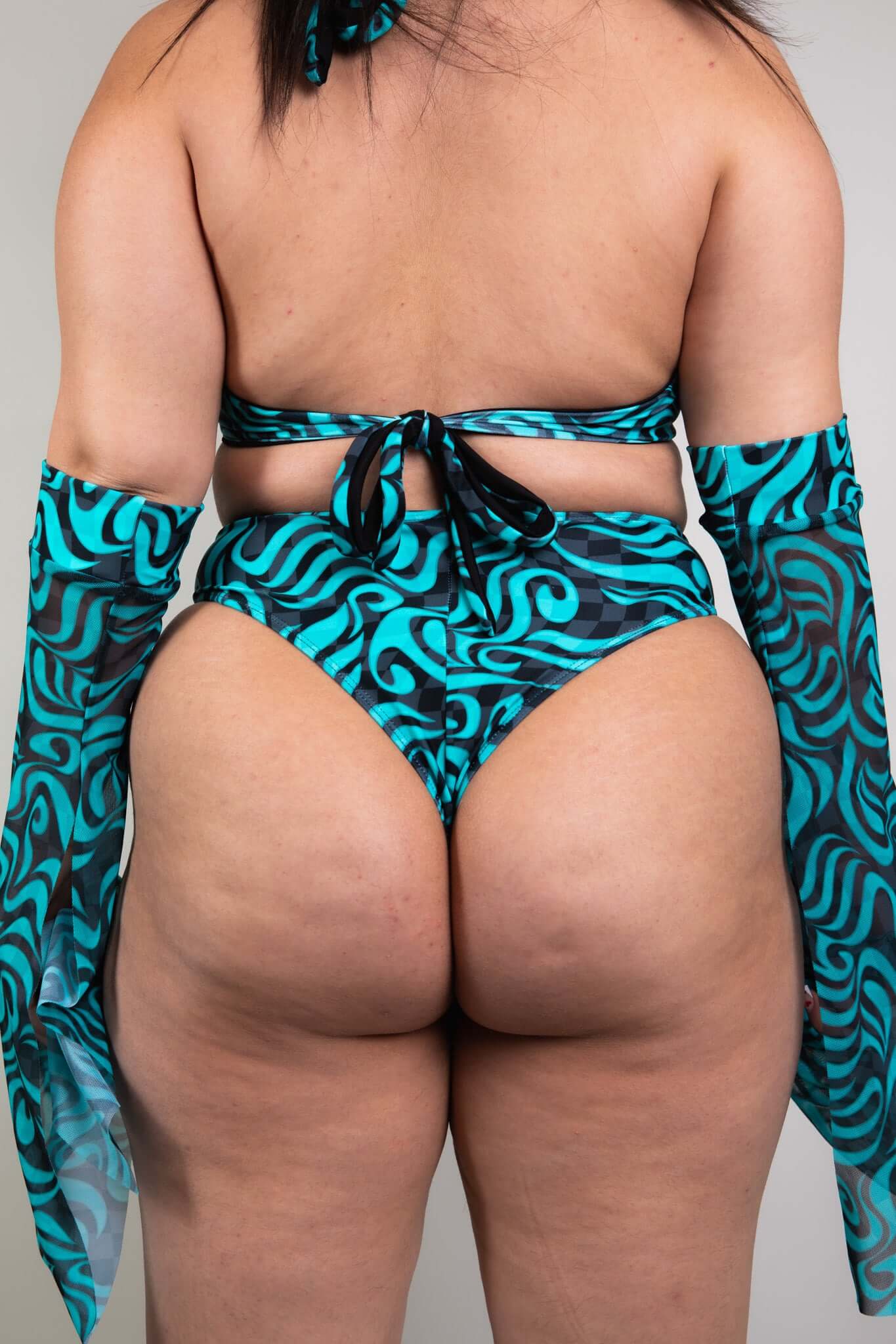 An up close photo of a woman wearing blue and black swirled bikini bottoms and a matching crop top. She is facing away from the camera.