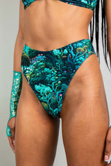 Close-up of a model in Freedom Rave Wear high-waisted bikini bottoms featuring a psychedelic forest print, paired with a matching top and shimmering arm sleeves