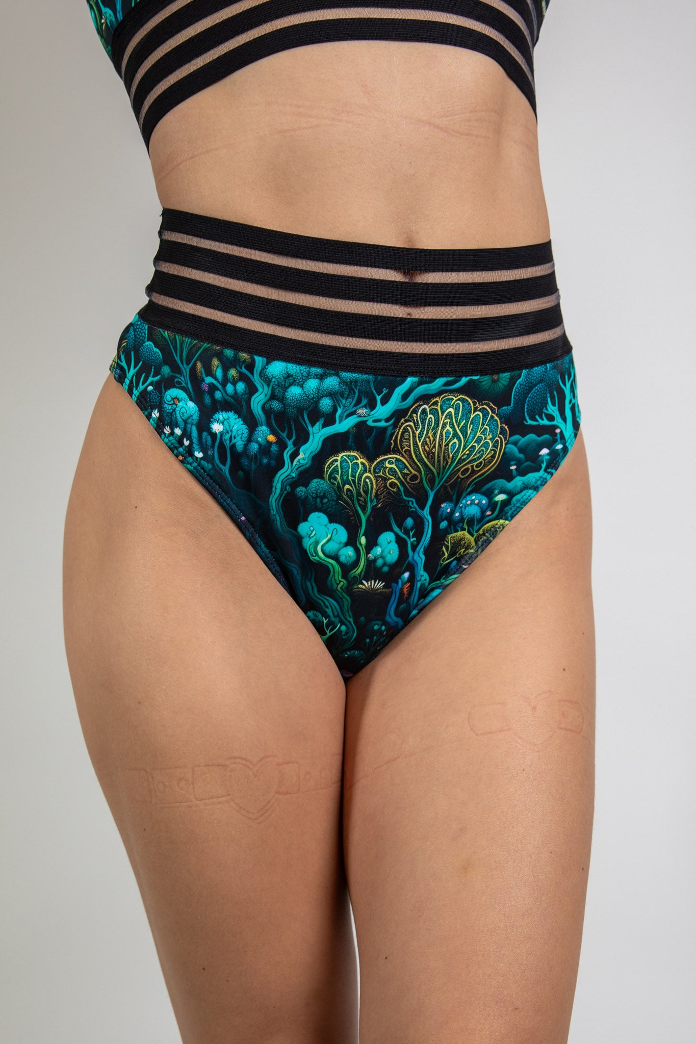 Faewood Sporty Bottoms in green and blue forest-inspired print, front view highlighting high-waist design and mesh stripe waistband.