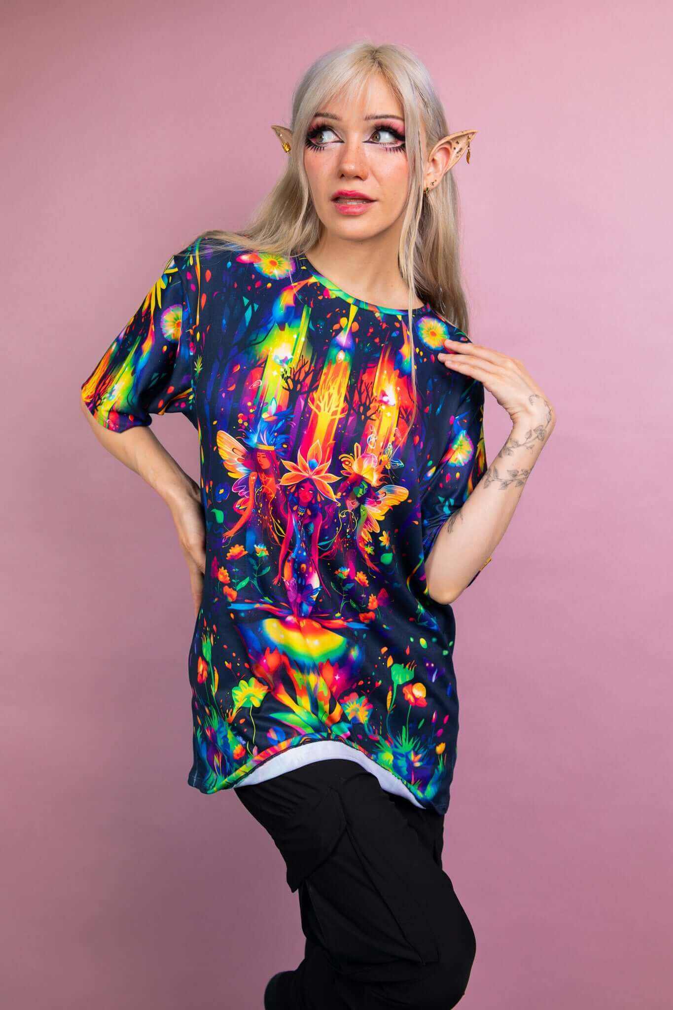 Model in a vibrant Freedom Rave Wear oversized tee with a fantasy forest design, paired with black pants, and fairy-inspired makeup and ears.