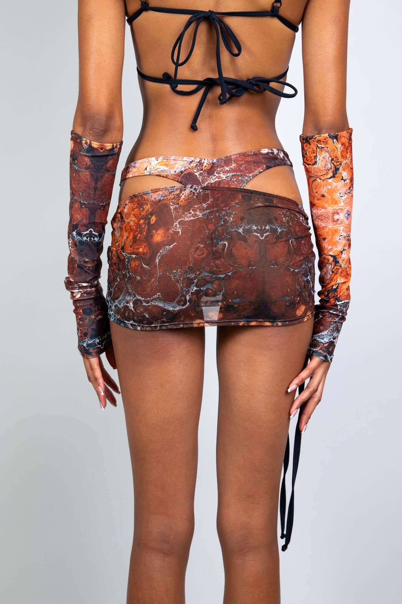 Back view of a brown sheer mini skirt with a detailed pattern and side straps from Freedom Rave Wear, paired with matching sleeves.