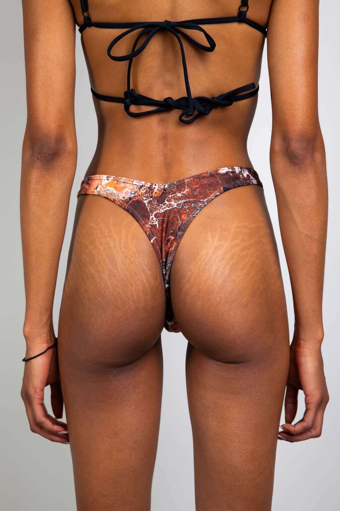 Rear view of a model wearing a brown and orange marbled bikini bottom from Freedom Rave Wear, showcasing the back design.