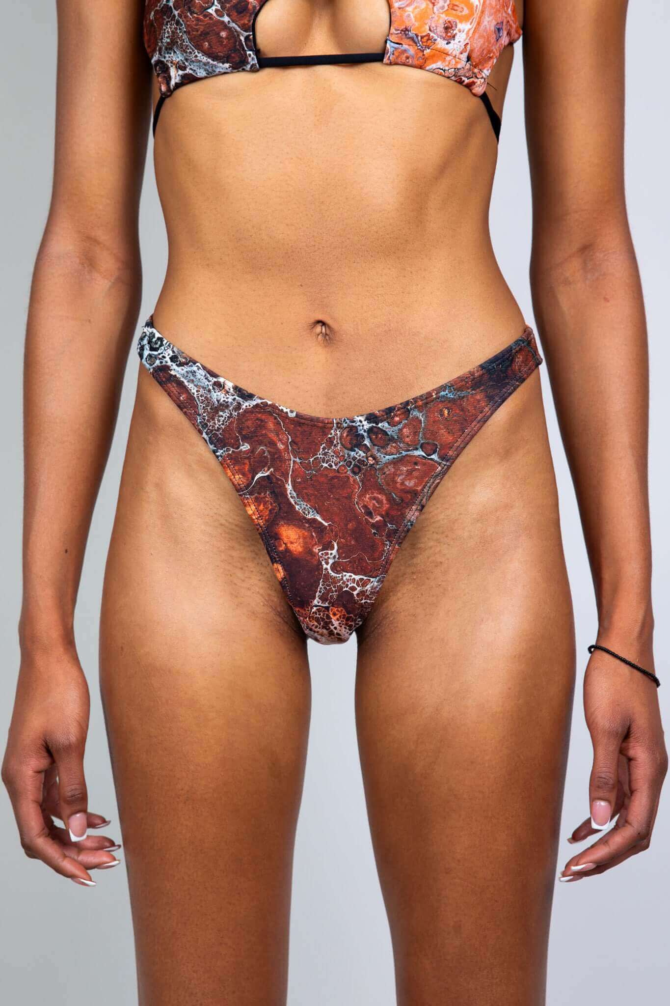 Close-up of a model wearing a brown and orange marbled bikini bottom from Freedom Rave Wear, showing a front view.