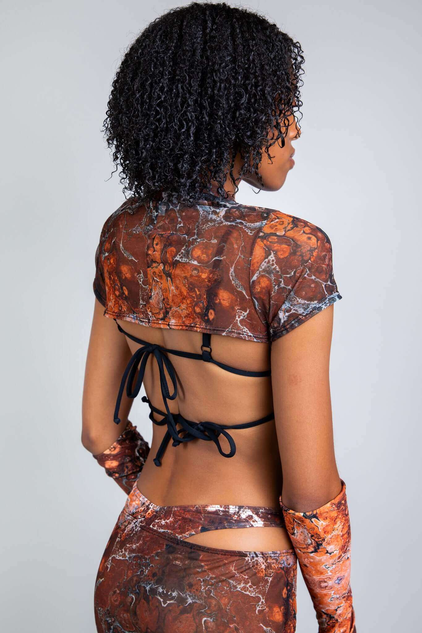 Model in a marbled brown and orange tie-back top and skirt set from Freedom Rave Wear, showcasing a side-back view.