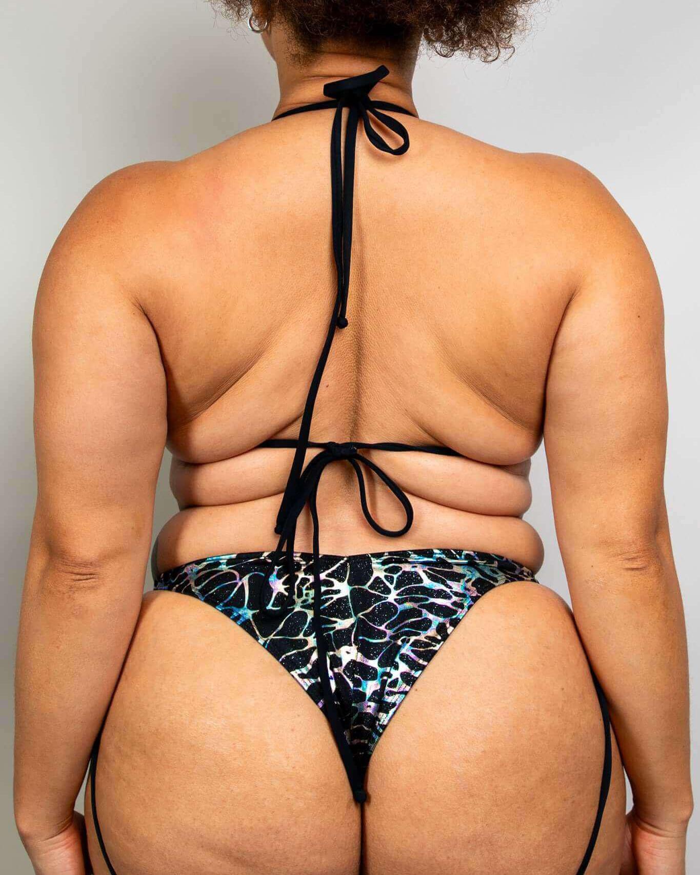 Back view of a plus-size model wearing the Galactica Strappy Bikini Top in black and oil slick design, perfect for rave outfits.