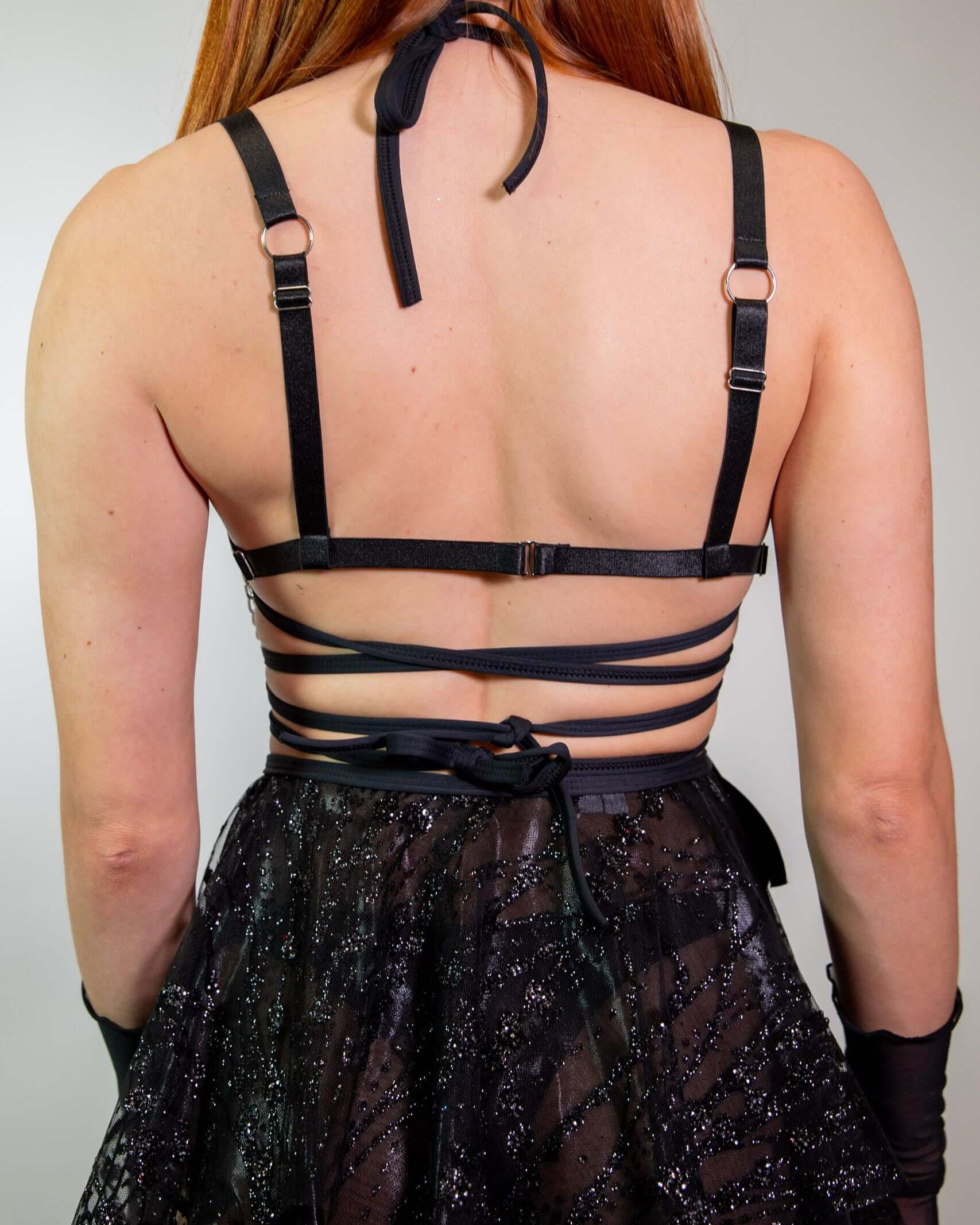 Back view of a woman wearing the Heartthrob Harness - Black, showcasing strappy details and a light chain design. Perfect for rave outfits.