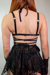 Back view of a woman wearing the Heartthrob Harness - Black, showcasing strappy details and a light chain design. Perfect for rave outfits.