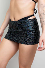 Model wearing a black holographic mini skirt by Freedom Rave Wear, showcasing an intricate swirling pattern with a high-waist fit, ideal for rave outfits