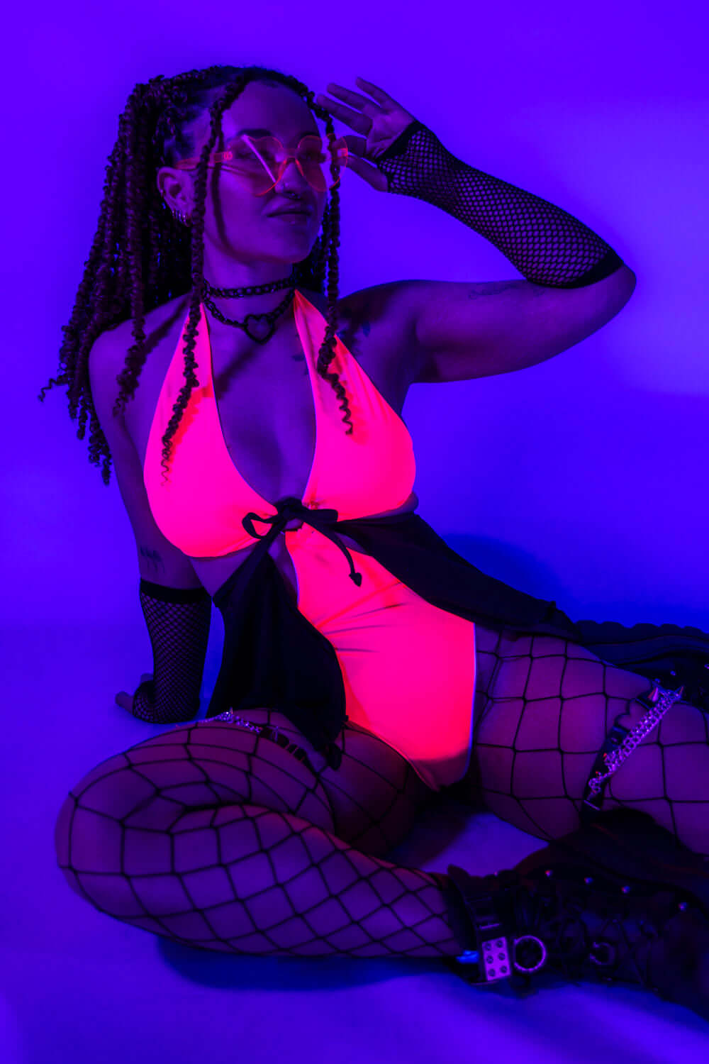 Neon-lit pose of the Hot Pink O-Ring Bodysuit, highlighting its glowing effect under blacklight.