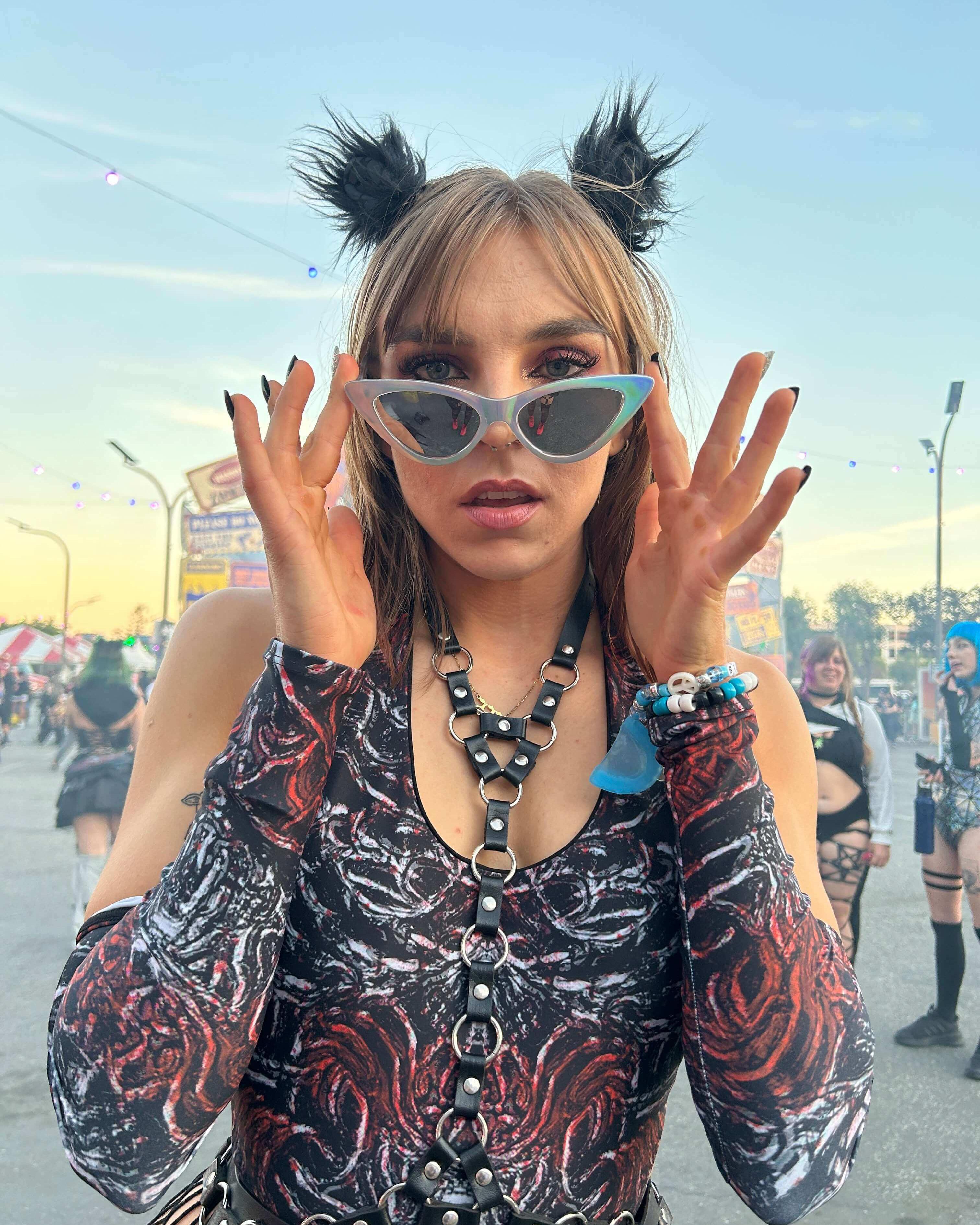 Woman in dark rave outfit with sunglasses and arm sleeves, embodying festival style and attitude.