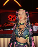 Model in a neon cyber rave outfit poses playfully at a bar with striking red neon lights in the background.