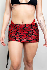 Model wearing the Inferno Cinch Skirt with adjustable ties in red and black flame pattern, perfect for rave outfits.