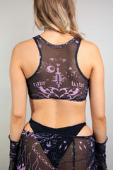 An up close photo of a woman wearing a mesh crop top. The top is black with purple tattoo-like designs on it. She is facing away from the camera.