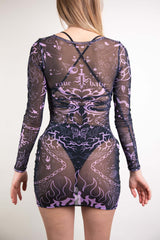 An up close photo of a girl wearing a short, fitted mesh dress with long sleeves. She is wearing a black bikini under the dress. The dress is black with purple tattoo inspired designs on it. The girl is facing away from the camera.