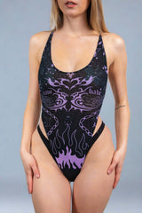 A photo of a woman wearing a scoopneck mesh bodysuit with black bikini bottoms. The bodysuit is black with purple tattoo-like designs on it.
