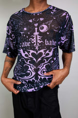 An up close photo of a man wearing a black mesh t-shirt with purple tattoo-like designs on it. He is wearing black pants.