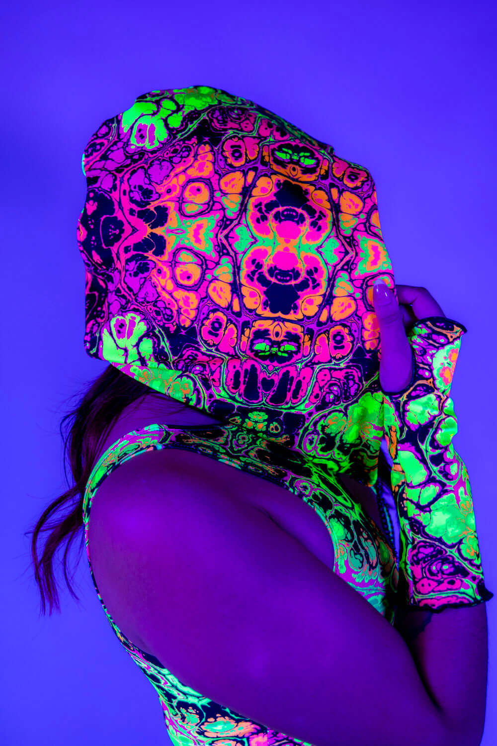 Woman wearing Intensity Assassin Hood with vibrant UV print, showcasing rave outfits style in a colorful setting.