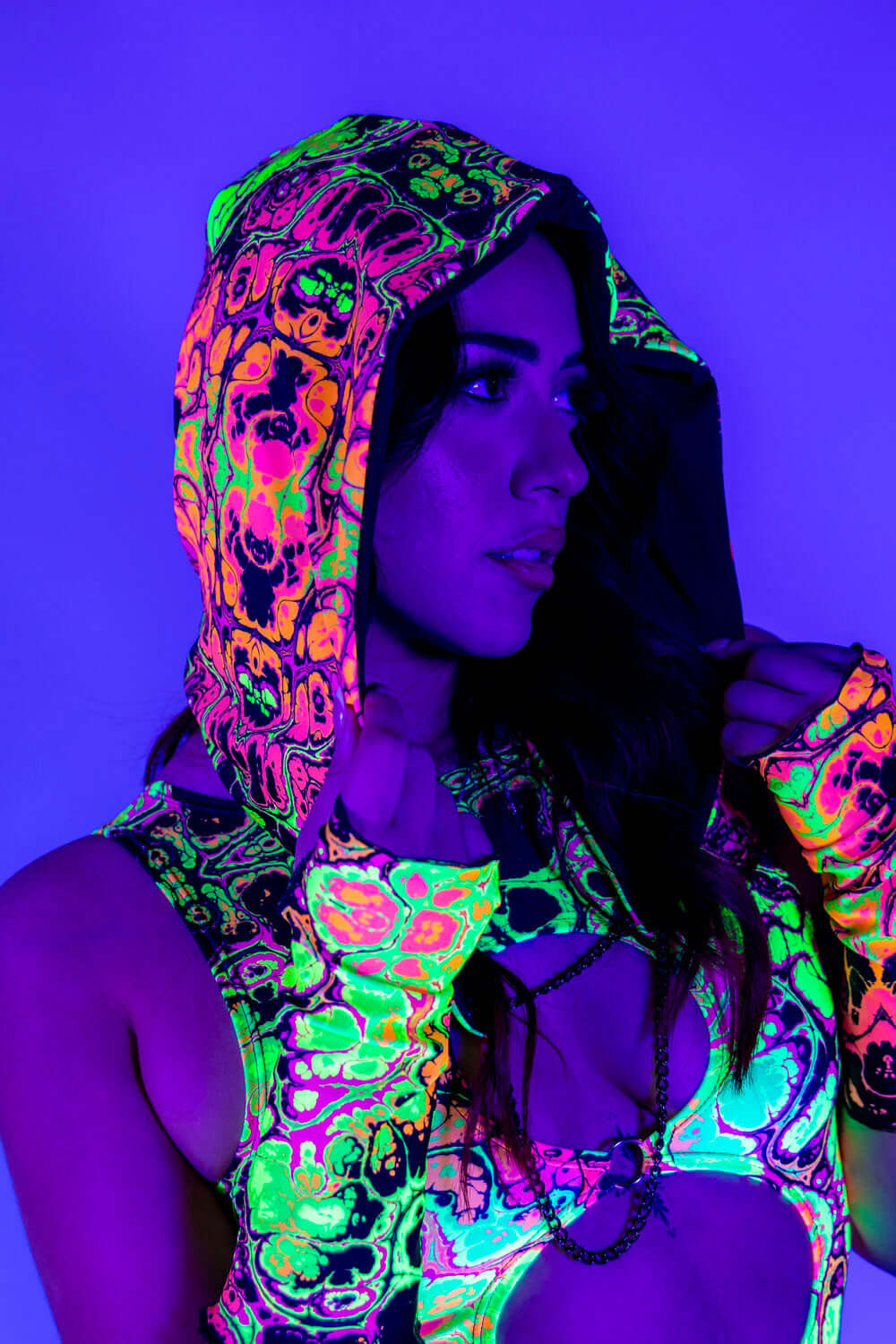 Model wearing Intensity Assassin Hood with vibrant UV print, showcasing stylish rave outfits under neon lighting.