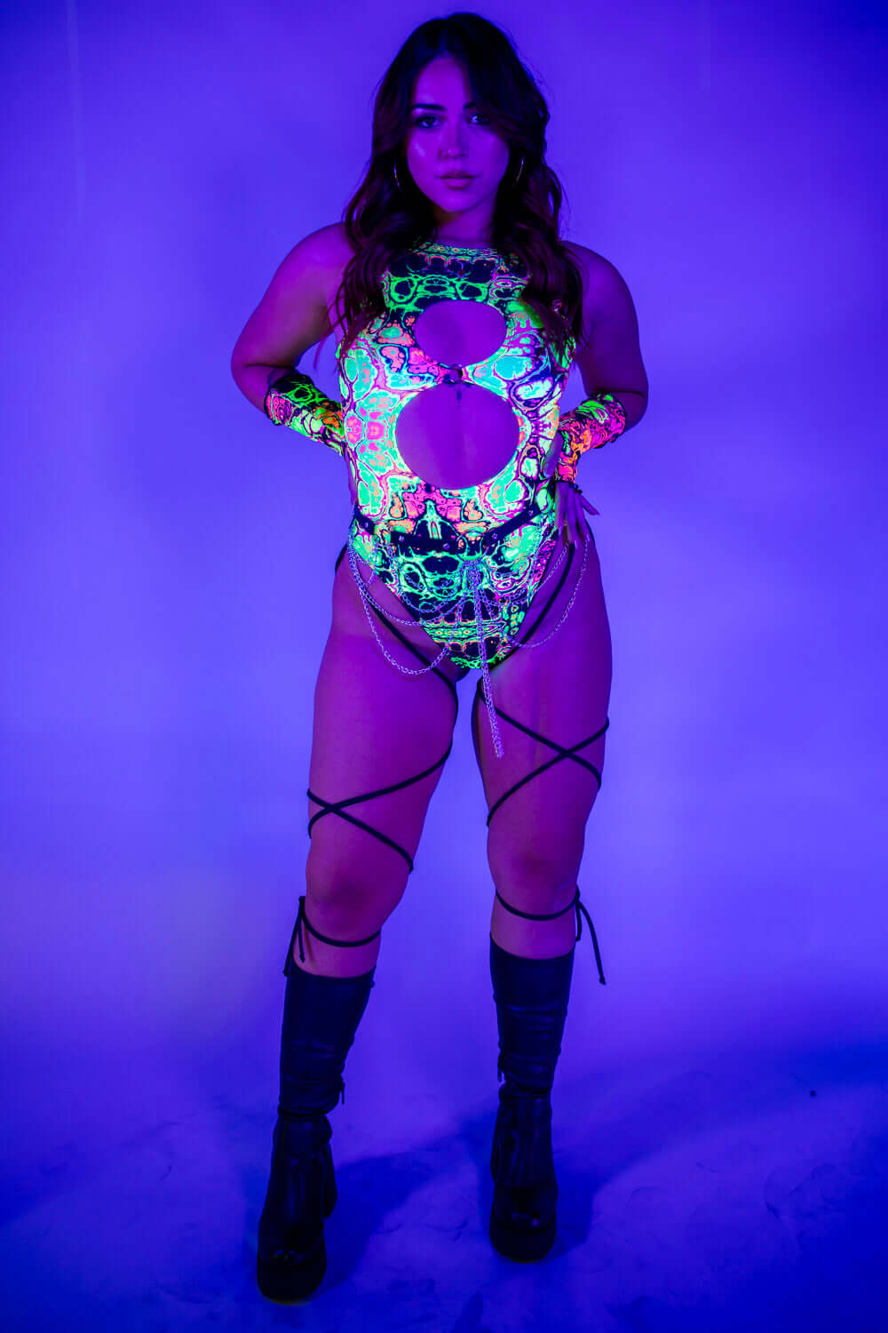 Model wearing Intensity Keyhole Bodysuit with leg straps, glowing under UV light, perfect for rave outfits.