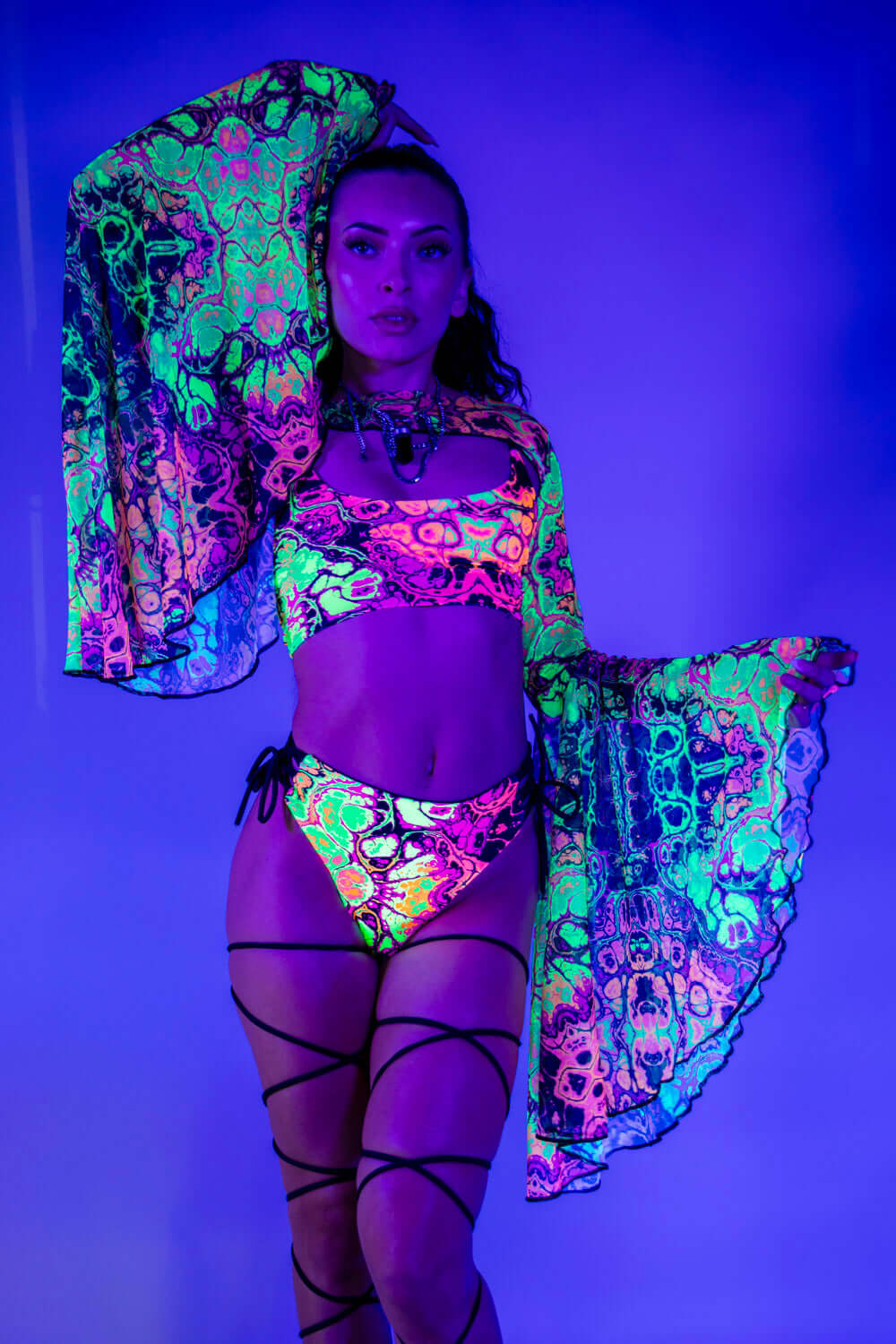 Model showcasing vibrant Intensity Mesh Bell Sleeves with UV reactive patterns, perfect for rave outfits.