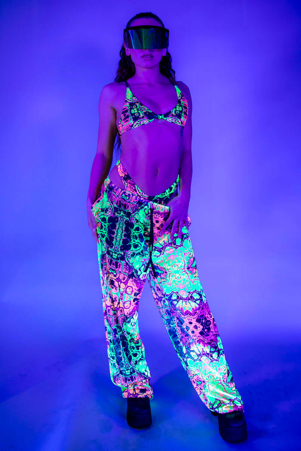 Front view of Intensity Mesh Lucy Pants under UV light, glowing in vibrant neon colors.