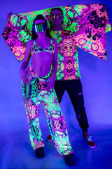 Couple in vibrant rave outfits with neon colors, glowing under UV light, showcasing unique fashion at a rave event.