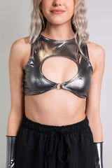 An up close photo of a woman wearing a chrome crop top with a keyhole cutout and black pants.