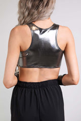 An up close photo of a woman wearing a chrome crop top and black pants. She is facing away from the camera.